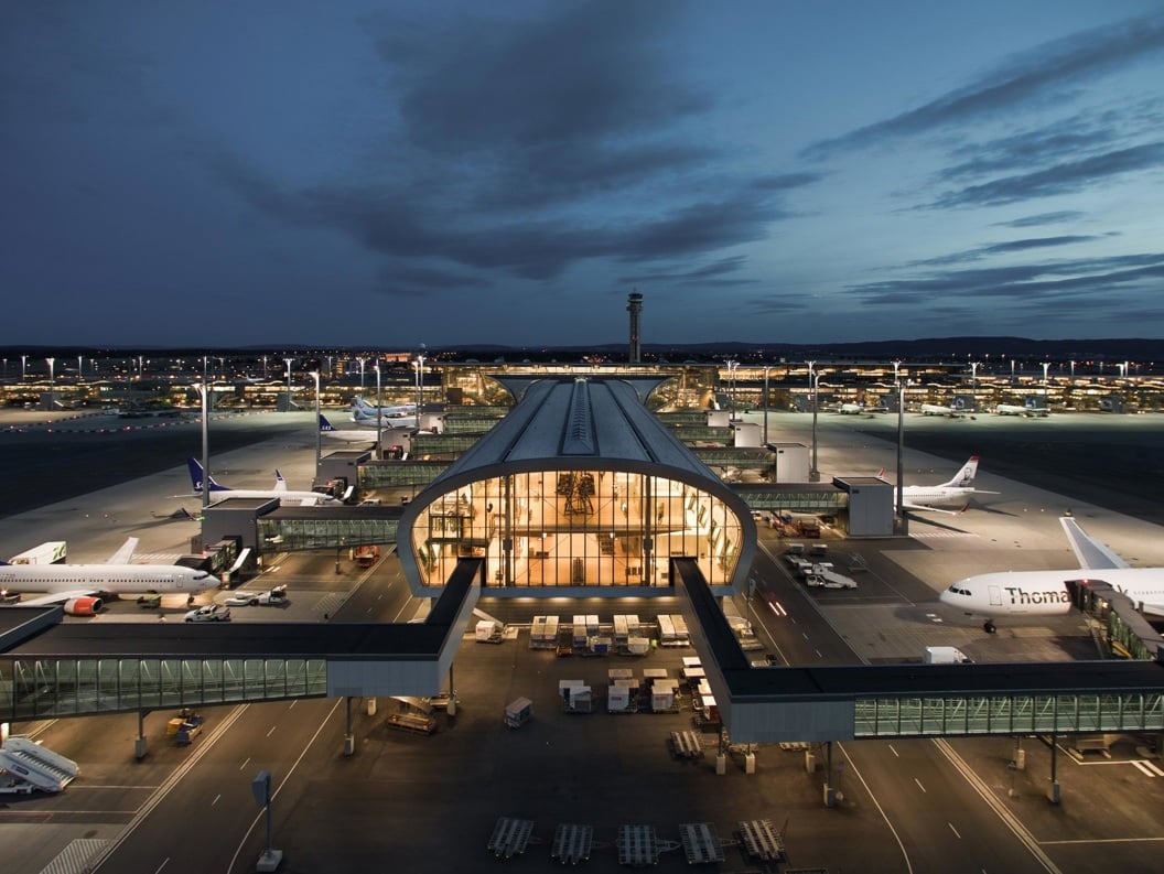 Airport at dusk with planes on the runway and terminal lighting.