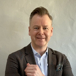 Smilende mann i dress med en uskarp moderne kontorbakgrunn
