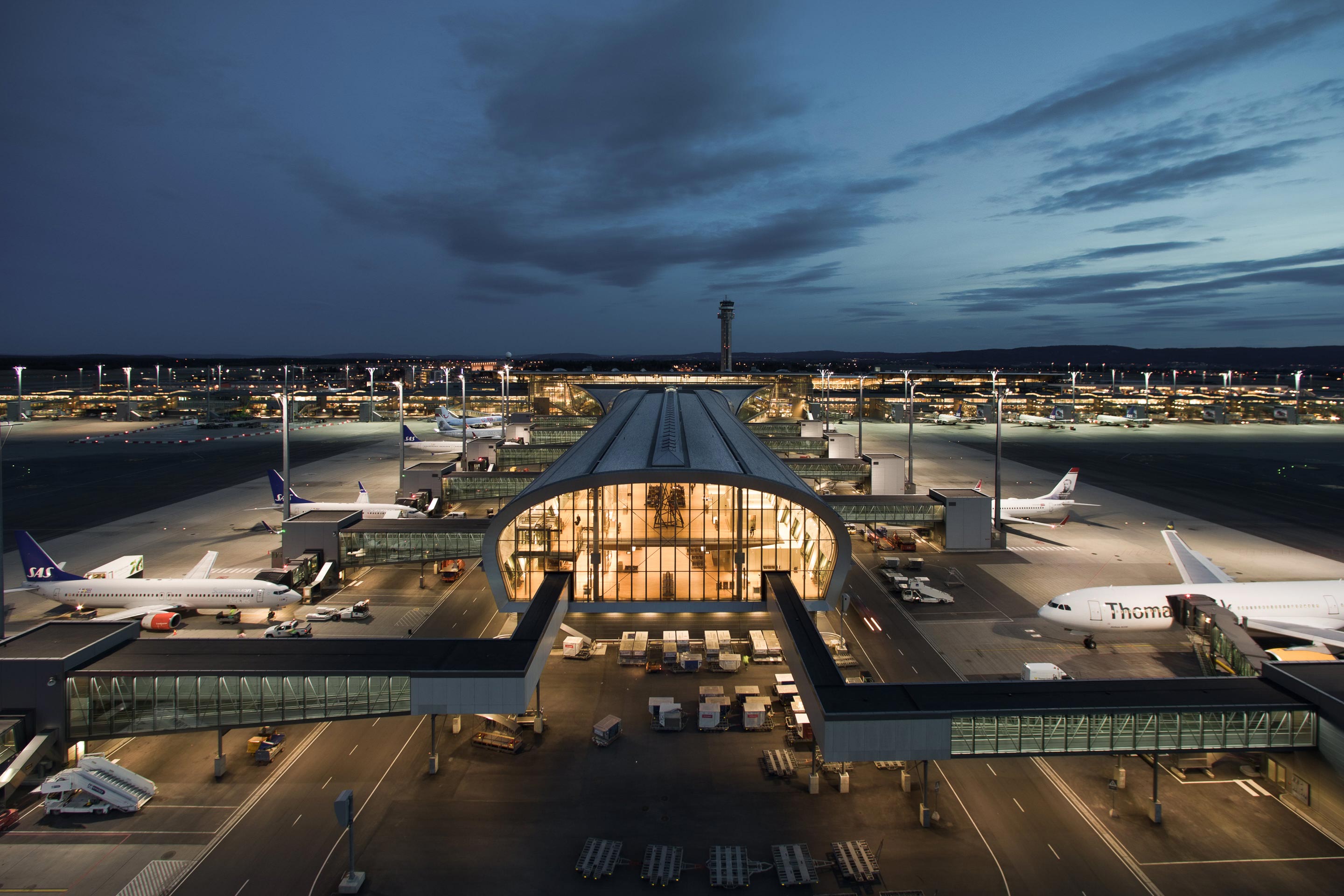Utsikt over Oslo lufthavn Gardermoen om kvelden, med flere fly parkert langs terminalen under opplyste forhold.
