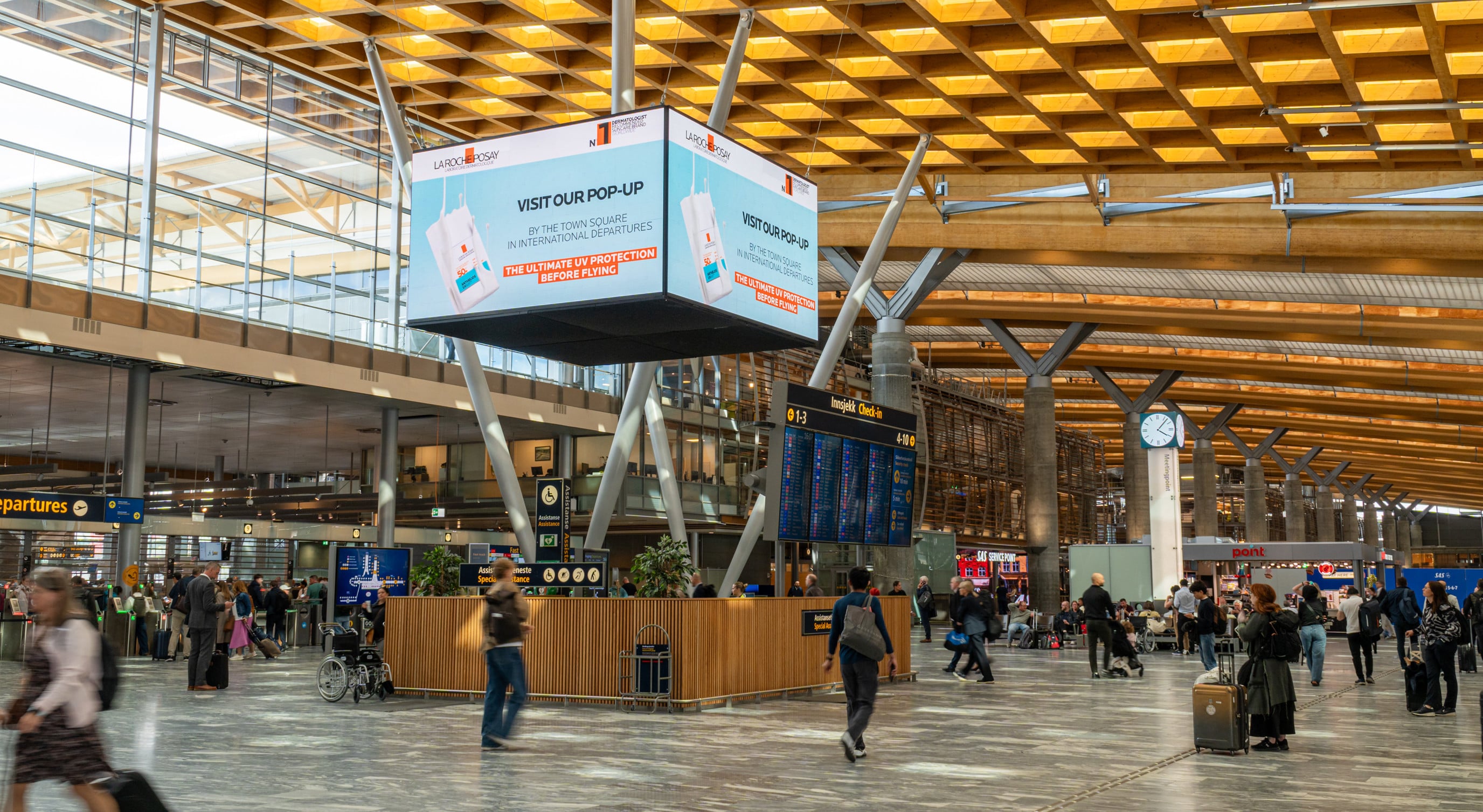 Flyplassterminal med reisende, informasjonsskjermer og reklameplakat for popup-butikk. Moderne arkitektur med store vinduer og trepanel i taket