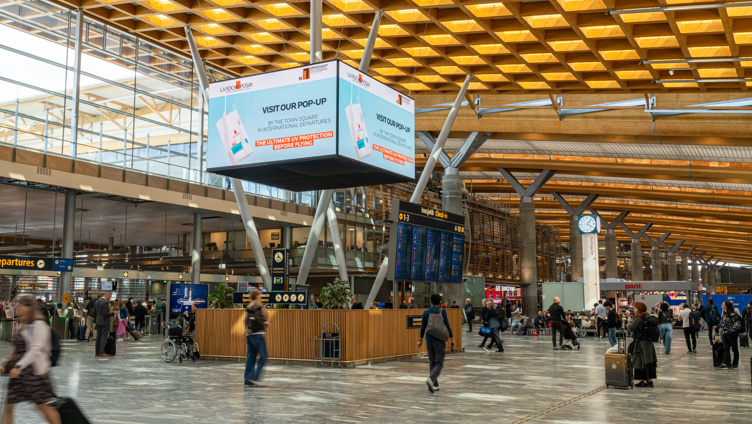 Flyplassterminal med reisende, informasjonsskjermer og reklameplakat for popup-butikk. Moderne arkitektur med store vinduer og trepanel i taket