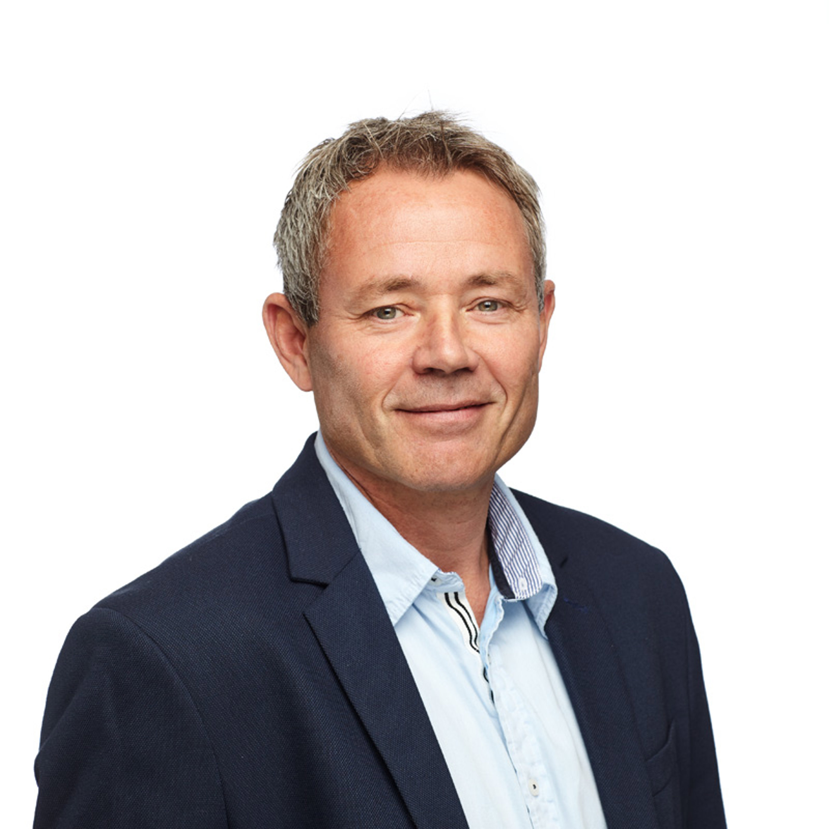 Mann i dressjakke og lyseblå skjorte smiler mot kameraet, med en nøytral bakgrunn.