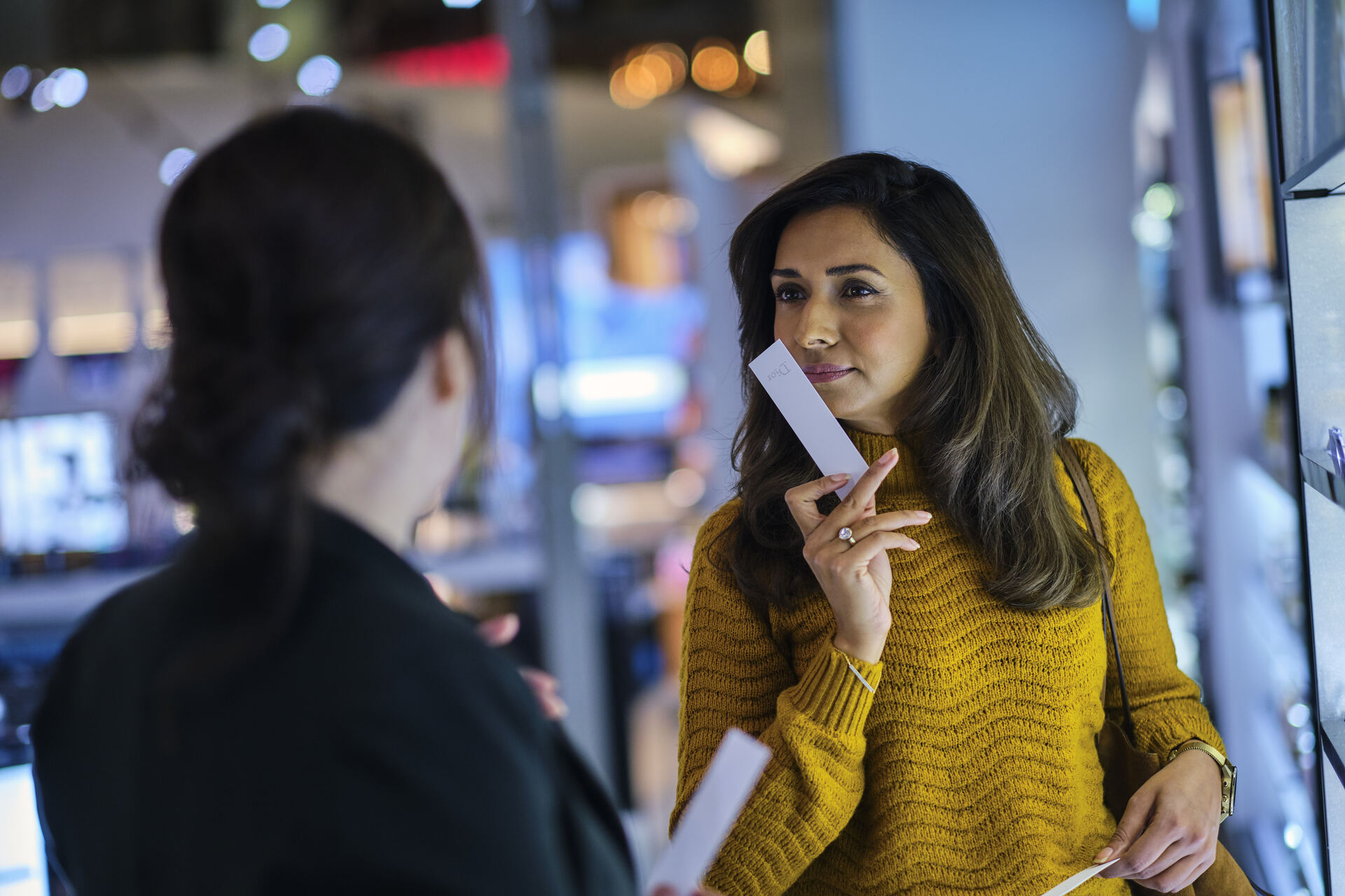 Woman wearing a yellow sweater smells a perfume sample in the store.