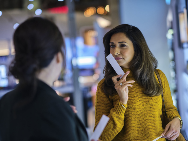 Woman wearing a yellow sweater smells a perfume sample in the store.