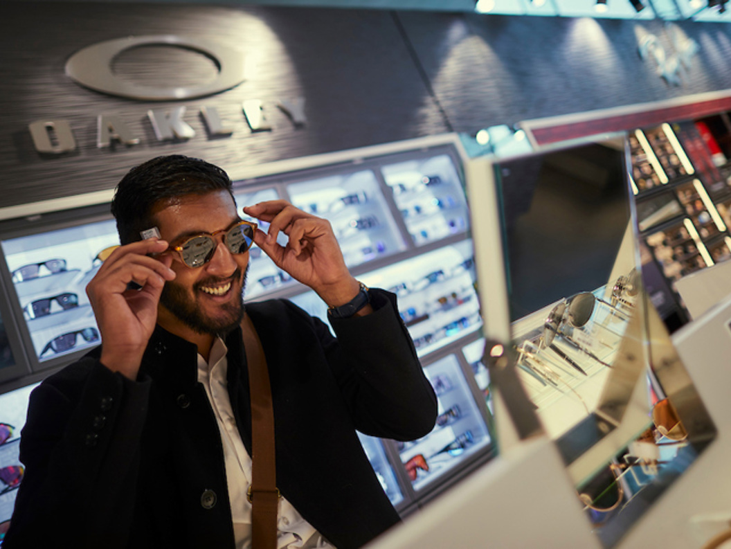 Mann prøver solbriller i en optikerbutikk, med Oakley-logo i bakgrunnen.