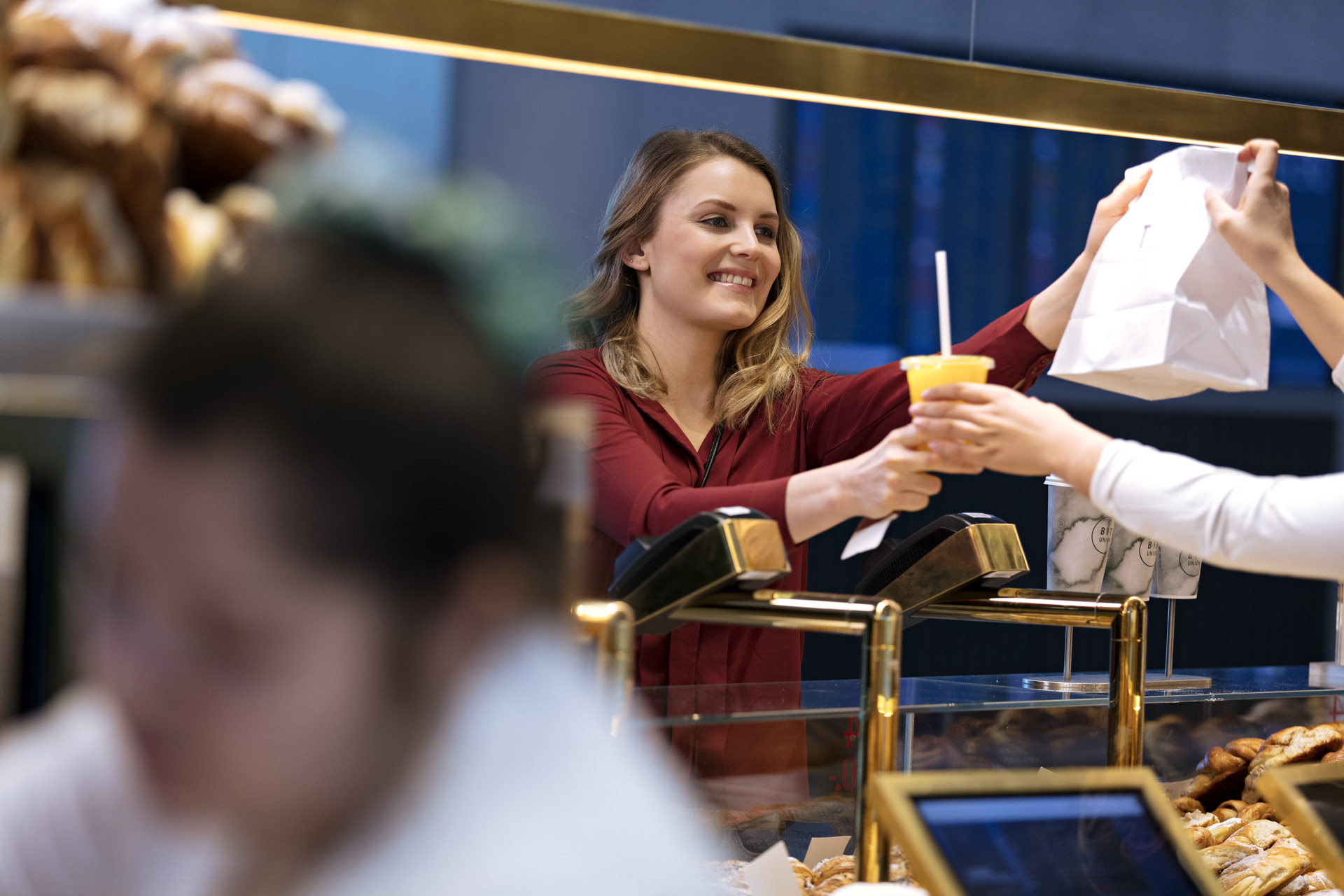 Woman in a café gives a customer a paper bag and a cold drink over the counter.
