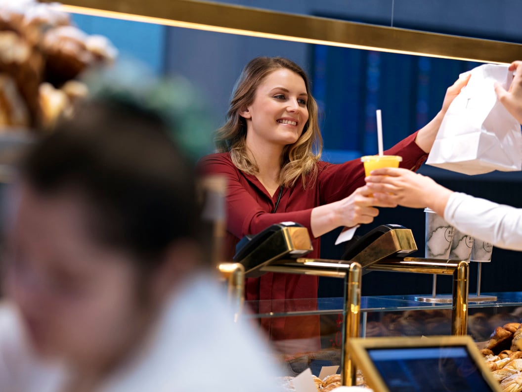 Woman in a café gives a customer a paper bag and a cold drink over the counter.