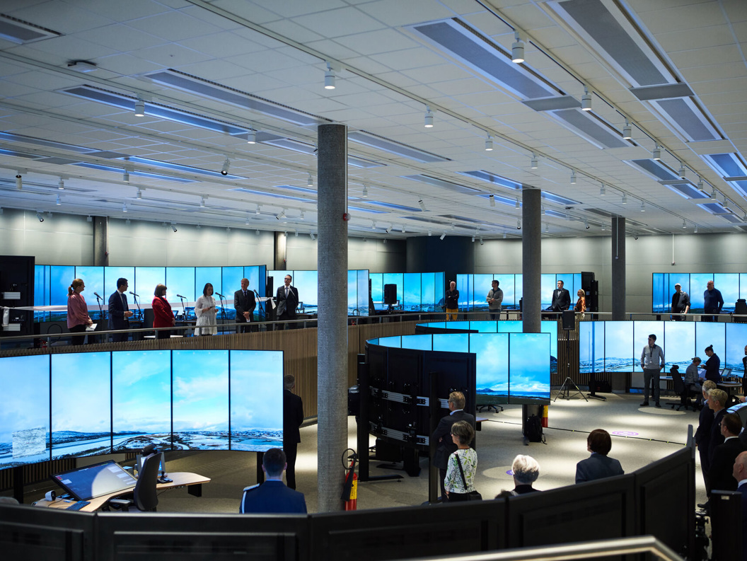 Spacious modern control room with multiple large display screens and staff members standing, showcasing operational monitoring and management.