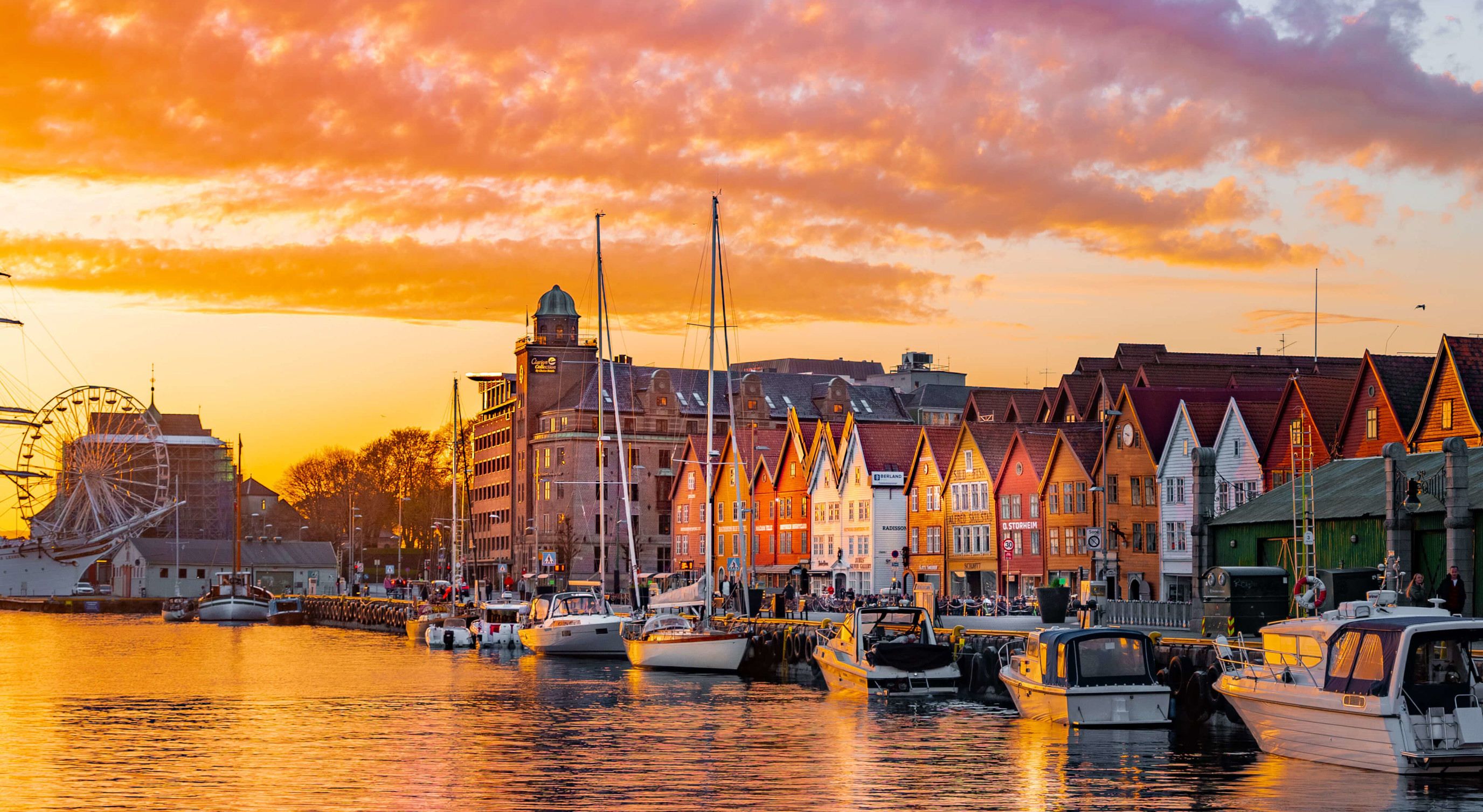 Bryggen i Bergen ved solnedgang med fargerike bygninger, båter i havnen og lysende skyer på himmelen.