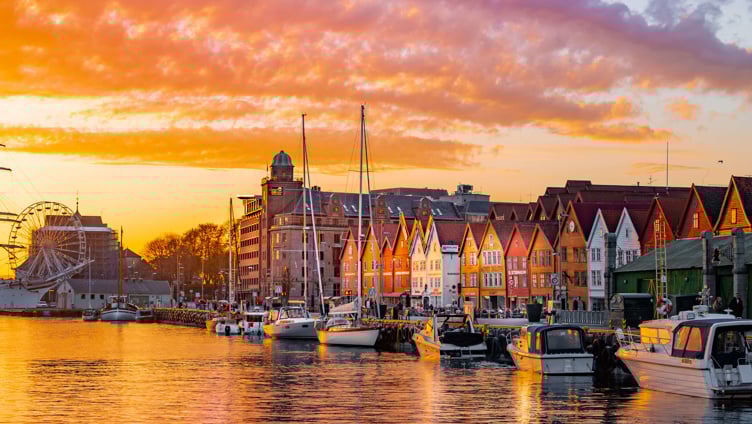 Bryggen i Bergen ved solnedgang med fargerike bygninger, båter i havnen og lysende skyer på himmelen.