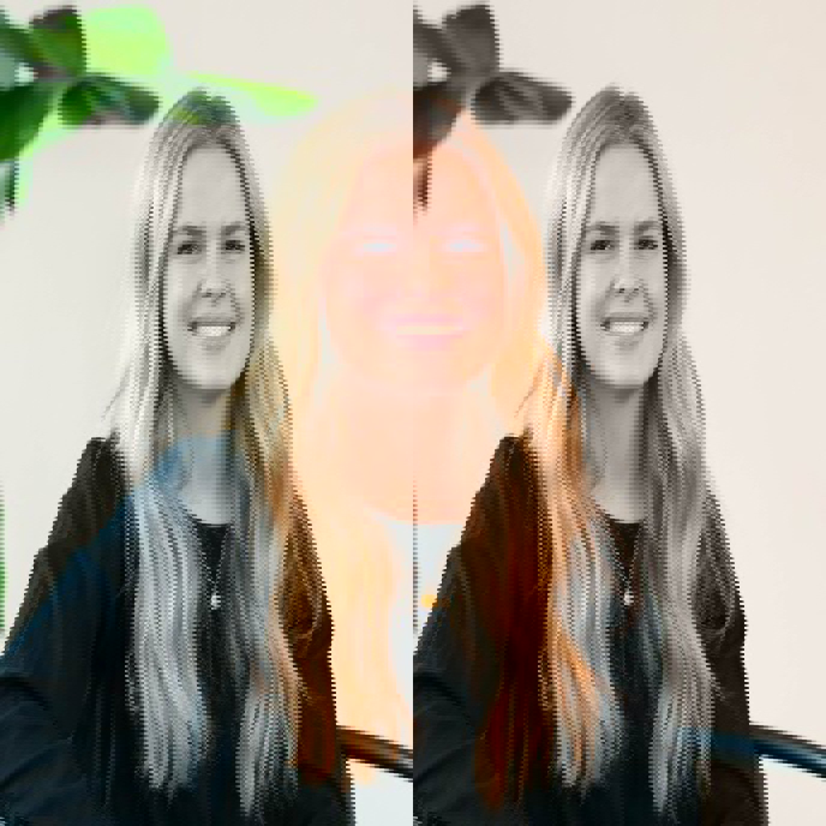 Smilende kvinne med langt blondt hår som har på seg en svart topp, sittende innendørs med en plante i bakgrunnen