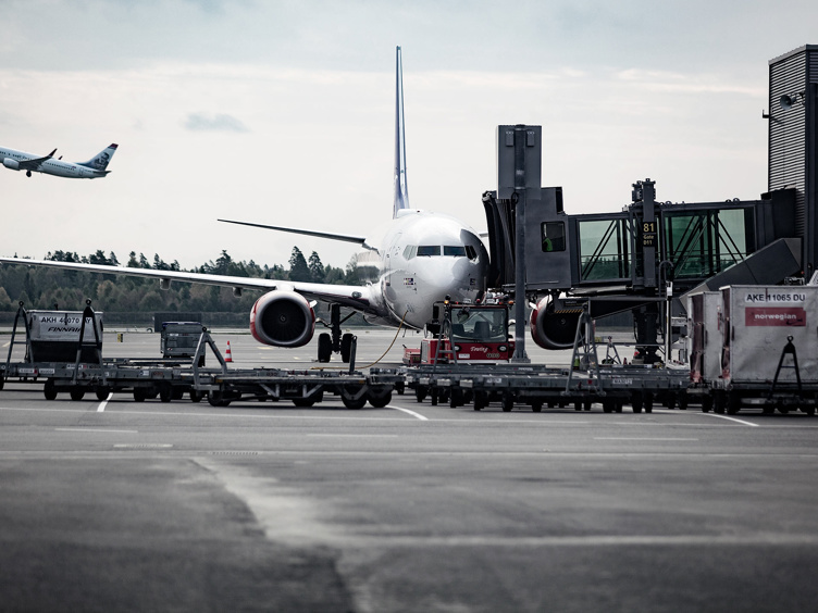 Fly ved flyplassgate med et annet fly som tar av i bakgrunnen, som viser travle flyplassoperasjoner og reiselogistikk