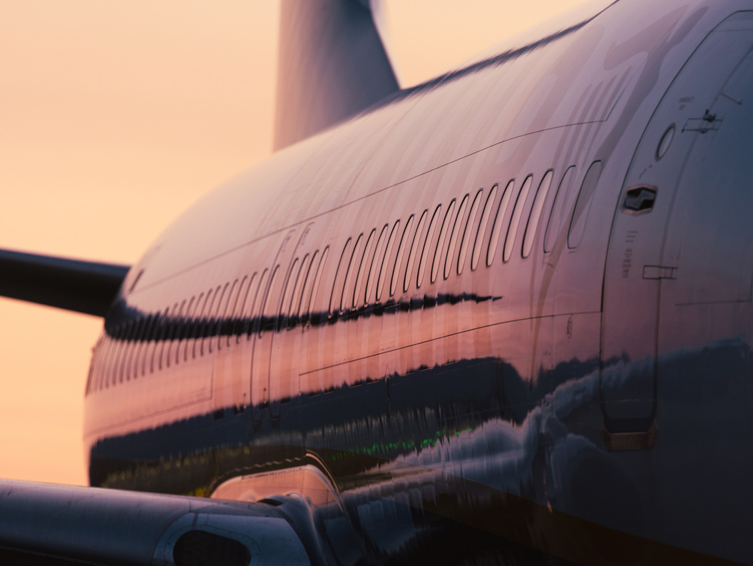 Sidebilde av et fly som reflekterer de varme fargene fra en solnedgang, og fremhever reise og luftfart