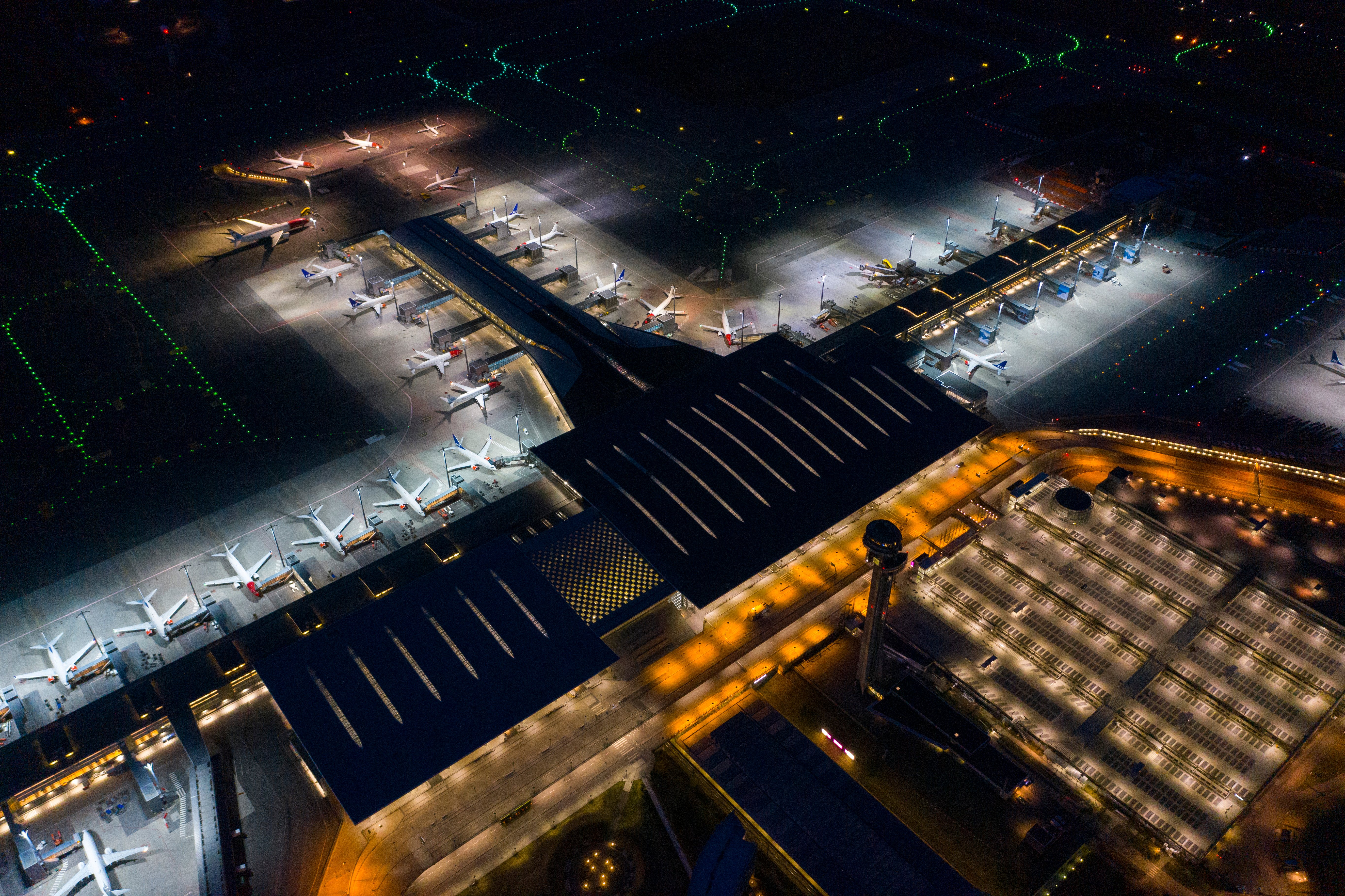 Aerial photo of a lit-up airport with parked planes and terminal building at night.