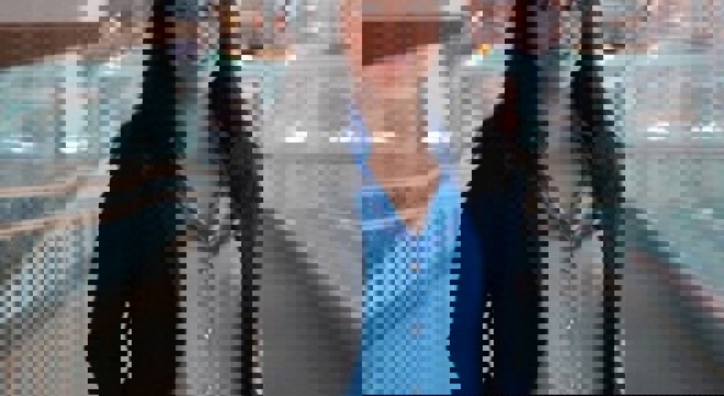 Kvinne i blå skjorte og mørk blazer står i en moderne bygning med glassvegger.