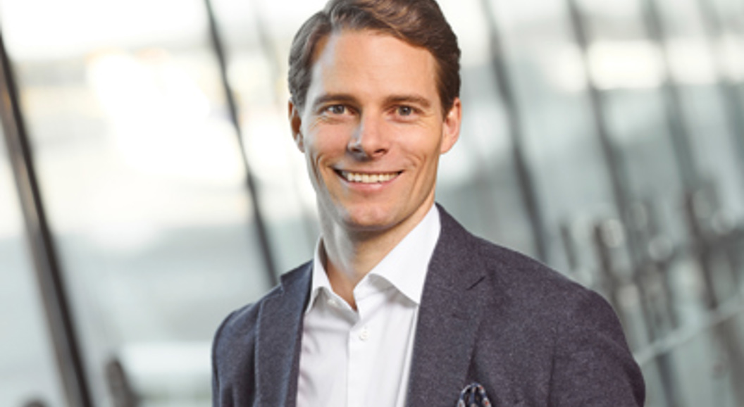 Smilende mann i dress med en uskarp moderne kontorbakgrunn