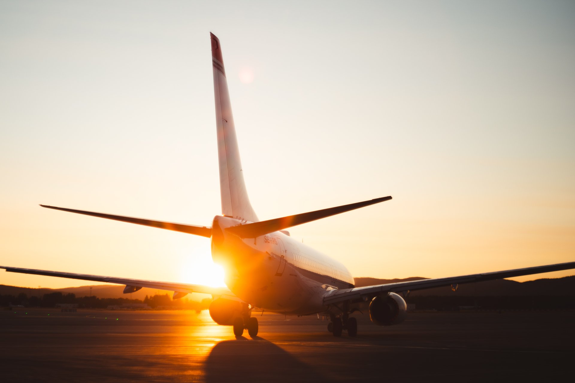 Kommersielt fly på rullebanen under soloppgang, fremhever silhuetten og den gyldne himmelen