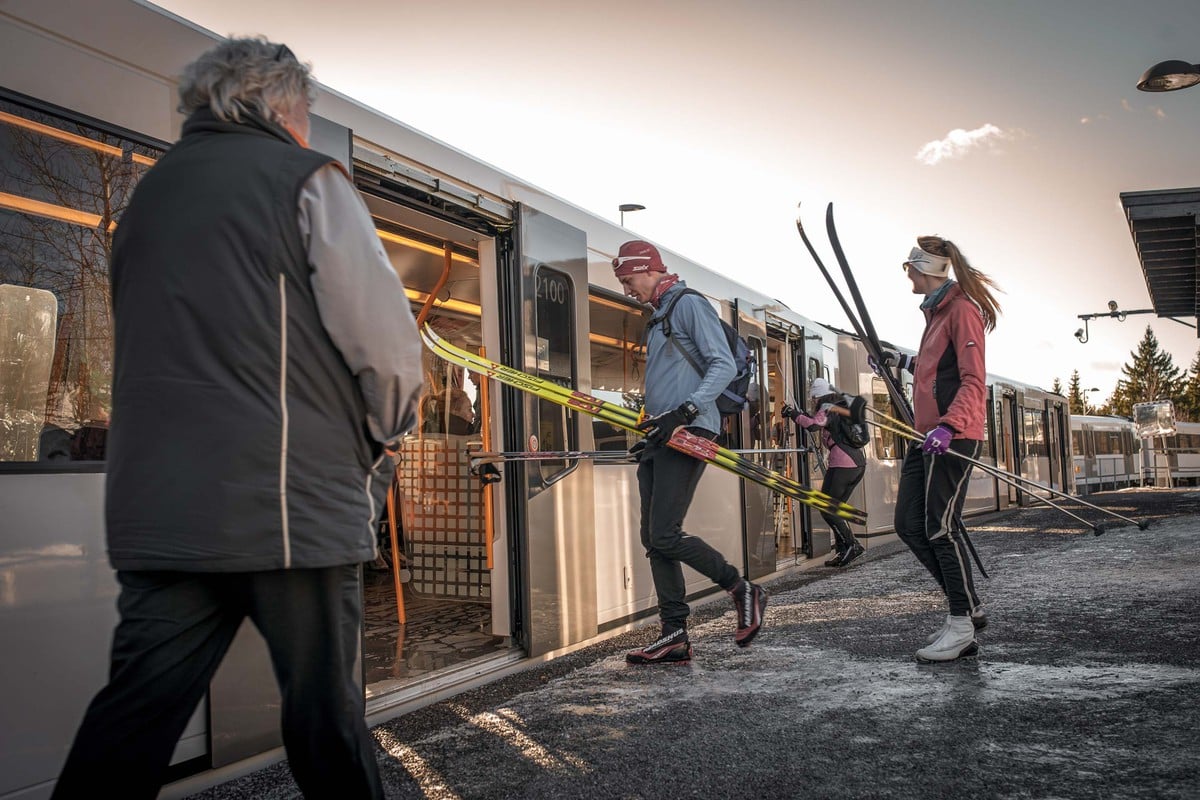 Personer med ski går ombord på en T-banevogn en vinterdag, klare for en skitur.