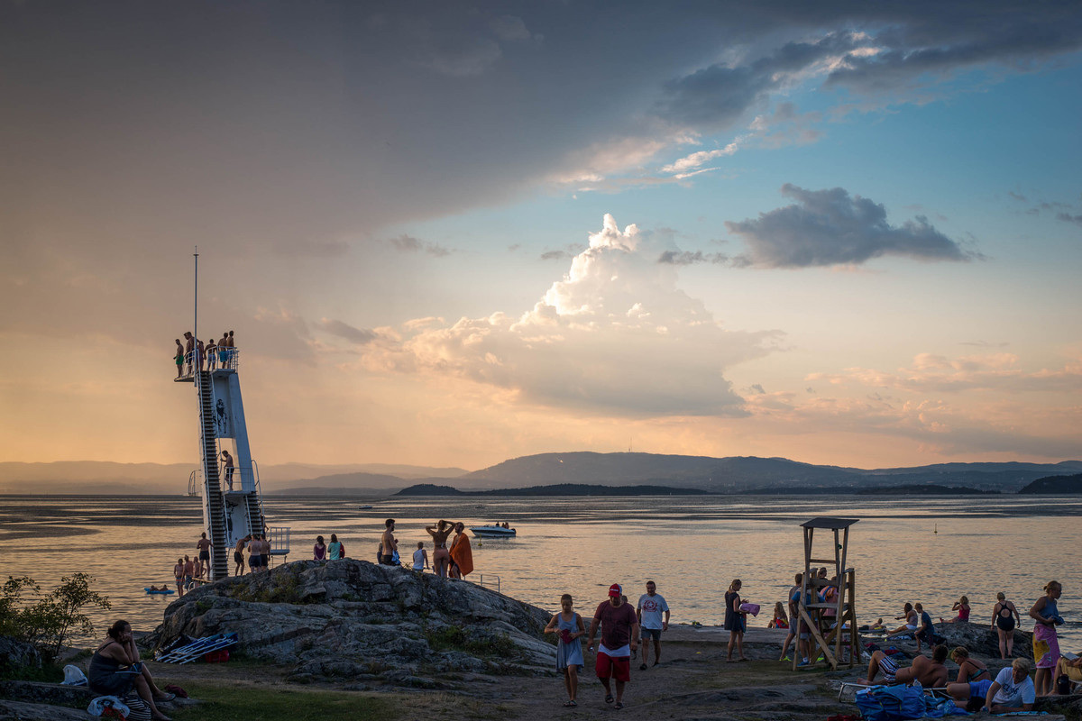 People gathered around and on a diving tower at Ingjerstrand in Oslo, sunset and blue sky in the background