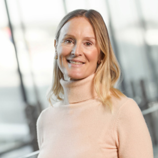 Smiling woman in a light pink turtleneck standing indoors with a blurred background