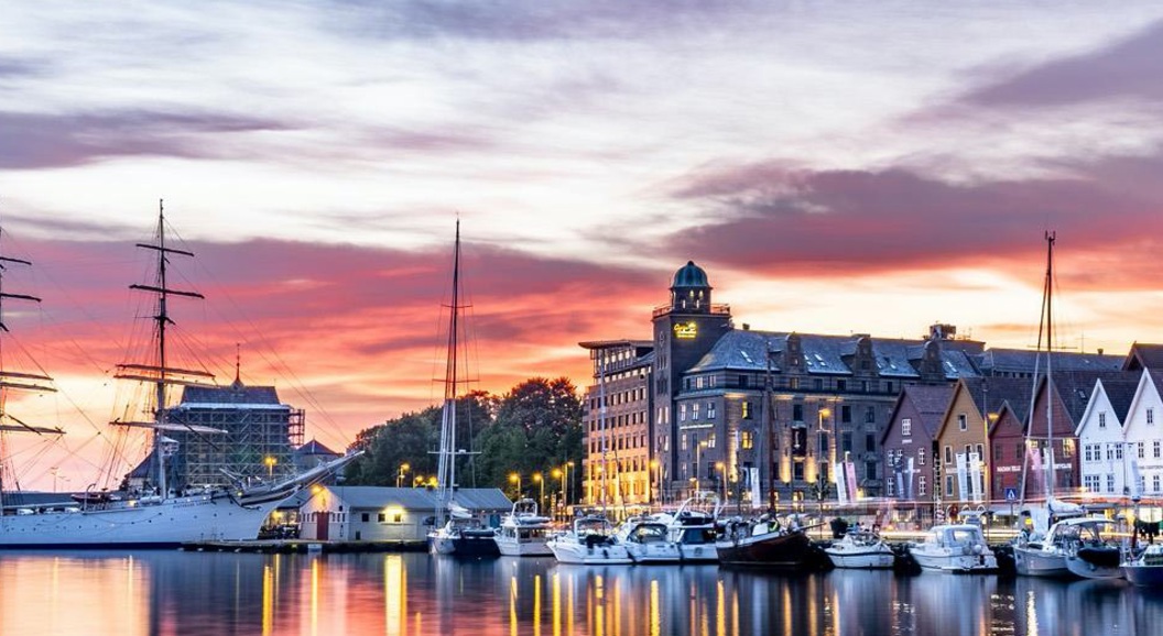Vakker utsikt over en havn med seilbåter og historiske bygninger ved solnedgang, med livlige himmelfarger og refleksjoner på vannet