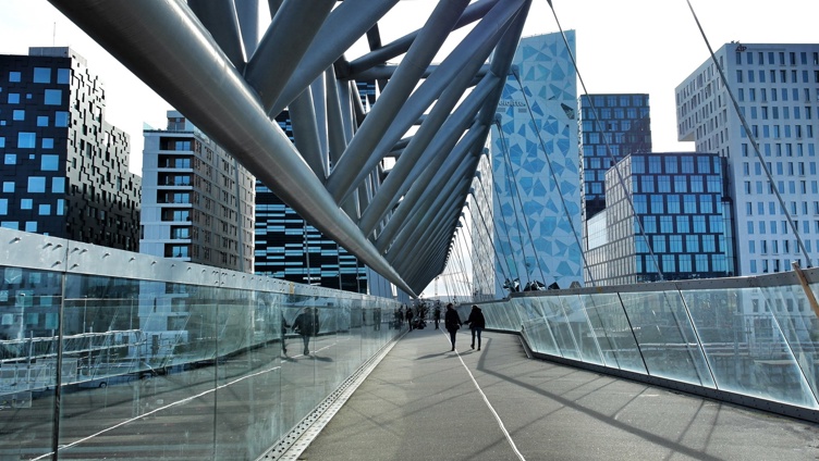 Gangbro med moderne arkitektur, med glassider og metallstøtter, omgitt av moderne høyhus i urbane omgivelser