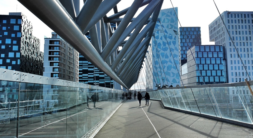 Gangbro med moderne arkitektur, med glassider og metallstøtter, omgitt av moderne høyhus i urbane omgivelser