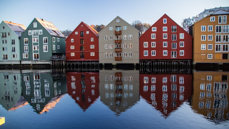 Fargerike trehus som speiler seg i en elv i Trondheim, Norge, på en klar dag