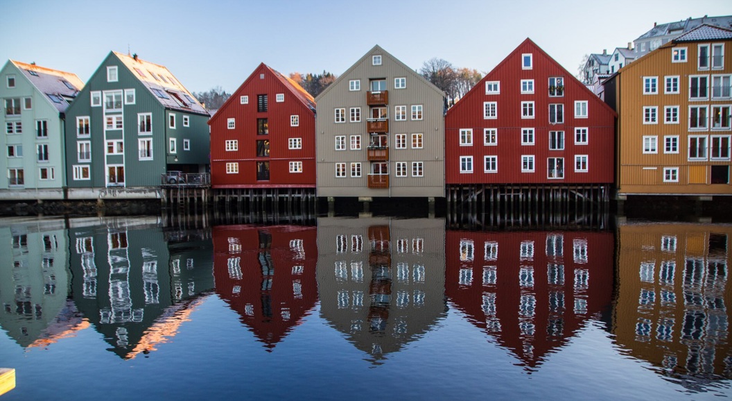 Fargerike trehus som speiler seg i en elv i Trondheim, Norge, på en klar dag