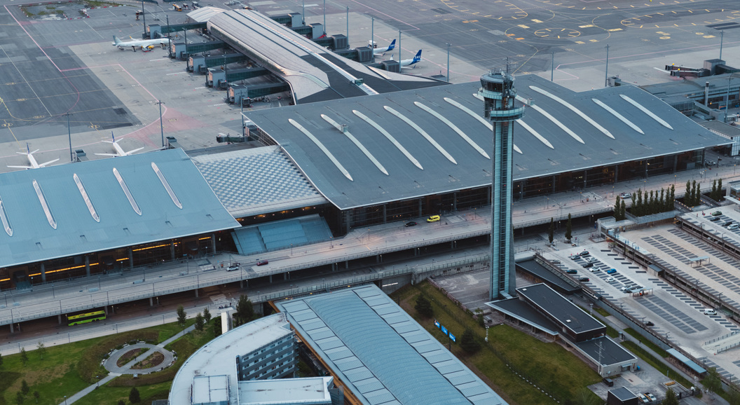 Flyplass med et stort passasjerfly parkert ved terminalen, byggkran i forgrunnen, og søknadsskjema med penn på bordet, symboliserer muligheter innen luftfartsindustrien.